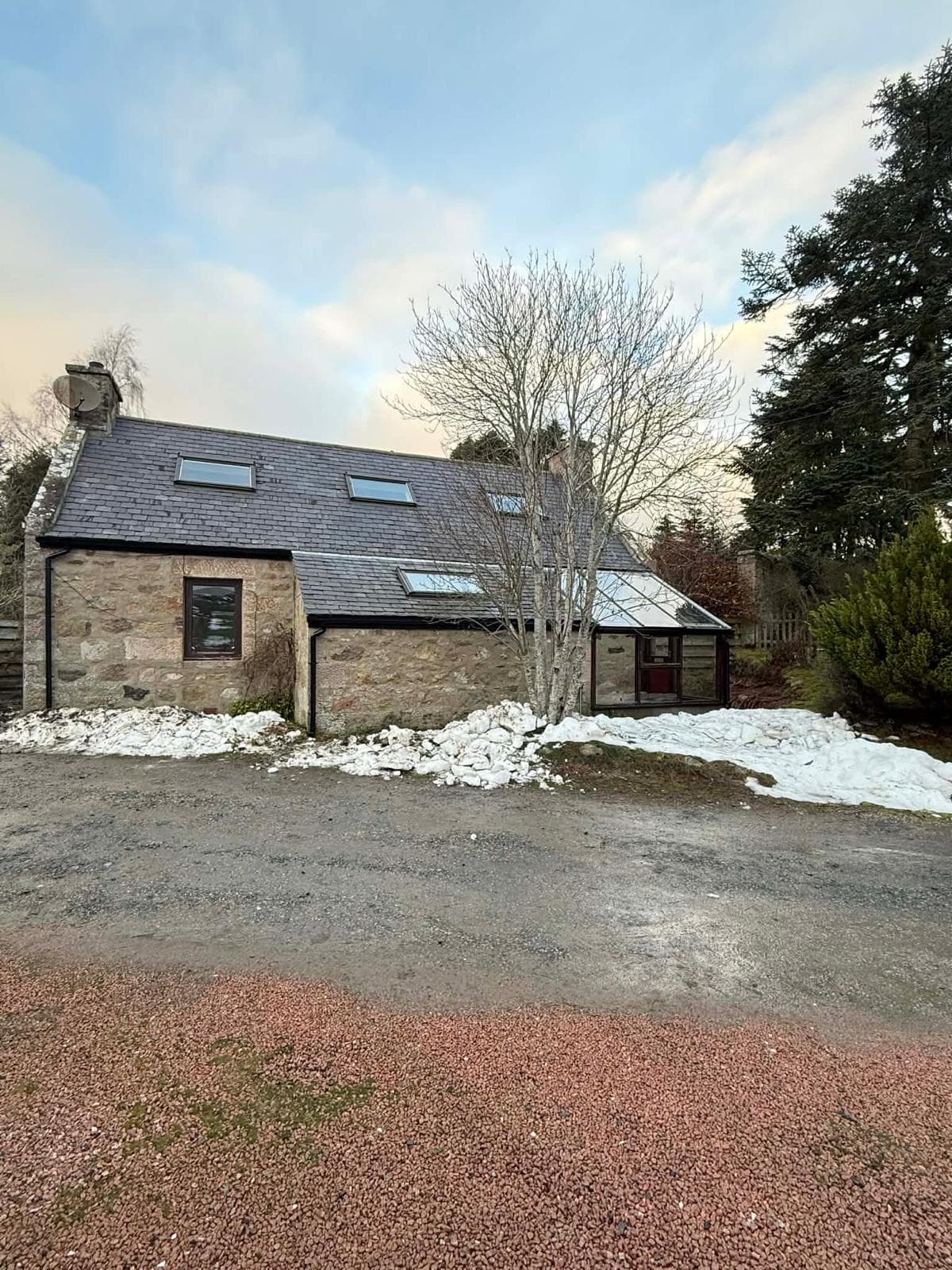 Slate roof and rooflights on a stone cottage with snow around the garden